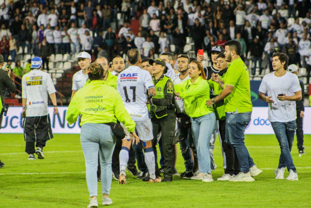 El personal de logística intenta conducir a Dayro Moreno hacía el camerino mientras él en la mitad de la cancha trata de hablar con los hinchas.