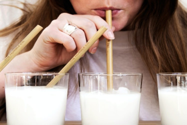 Mujer bebe leche de un vaso con un pitillo que sostiene con una mano.