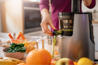 Mujer preparando jugo con muchas frutas y un extractor de jugo en una mesa.