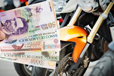 Mano sosteniendo billetes de pesos colombianos frente a varias motos.