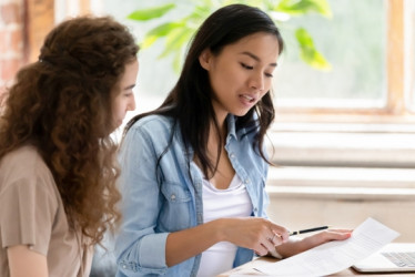 Dos mujeres sentadas en un escritorio revisando unos papeles.