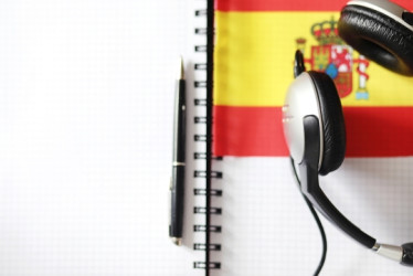 Cuaderno con un lapicero, audífonos y una bandera de españa